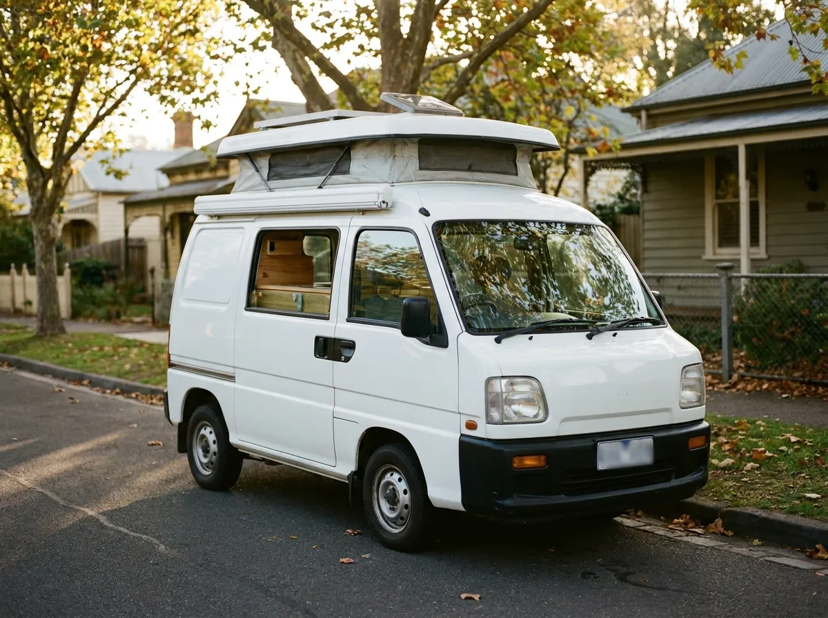 Furgoneta camper compacta con techo elevable aparcada en una calle residencial, luz cálida de atardecer