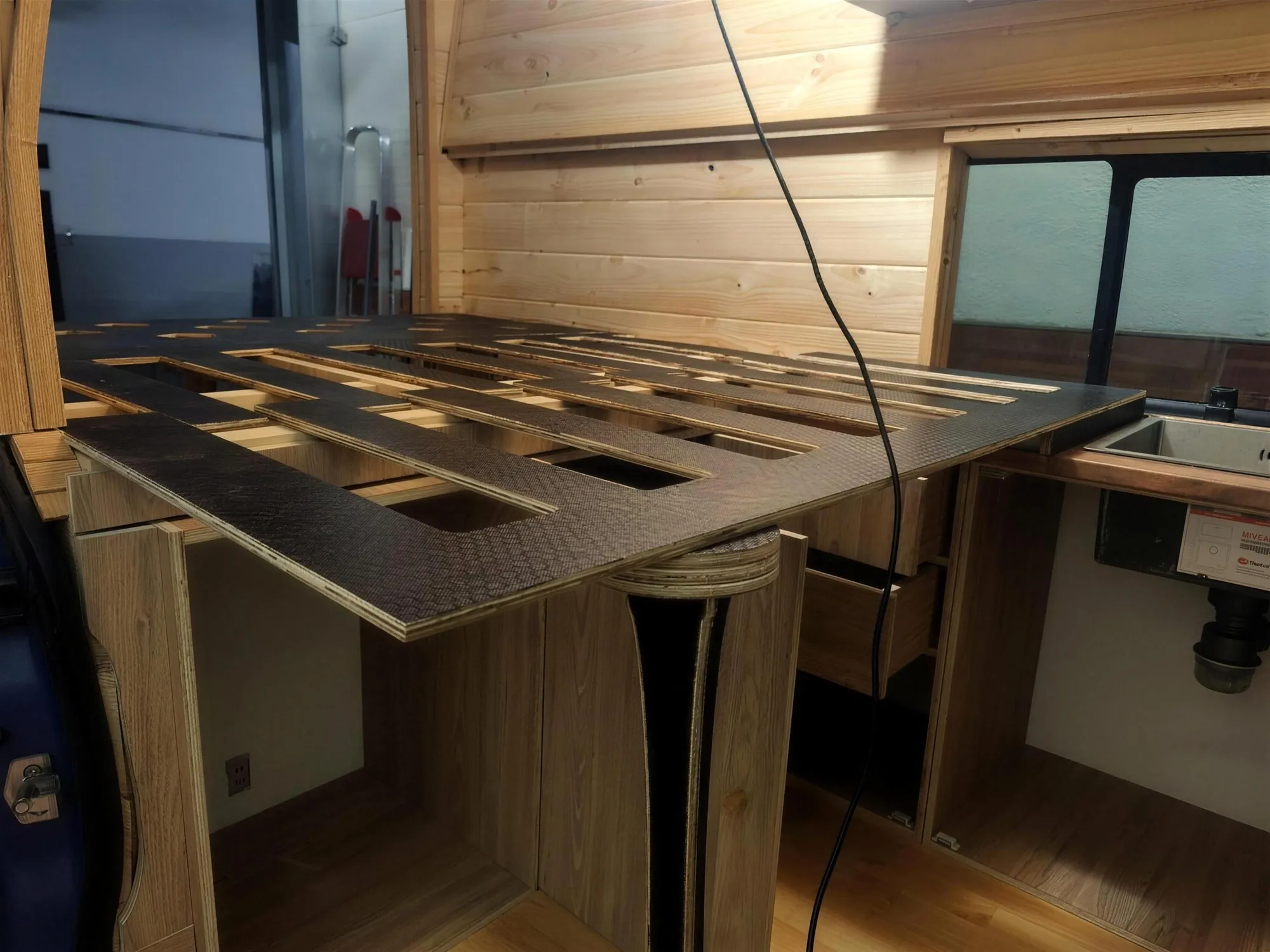 Módulo de cama y cocina en construcción dentro de una furgoneta camperizada, con el cableado eléctrico y el fregadero ya instalados